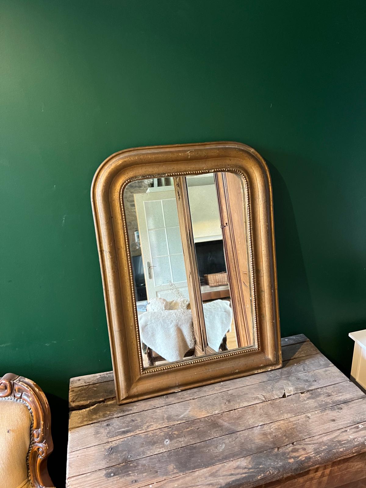 La Ferme Anglaise antique French Louis Philippe gilt mirror with a beaded border and foxed glass on a wooden surface.