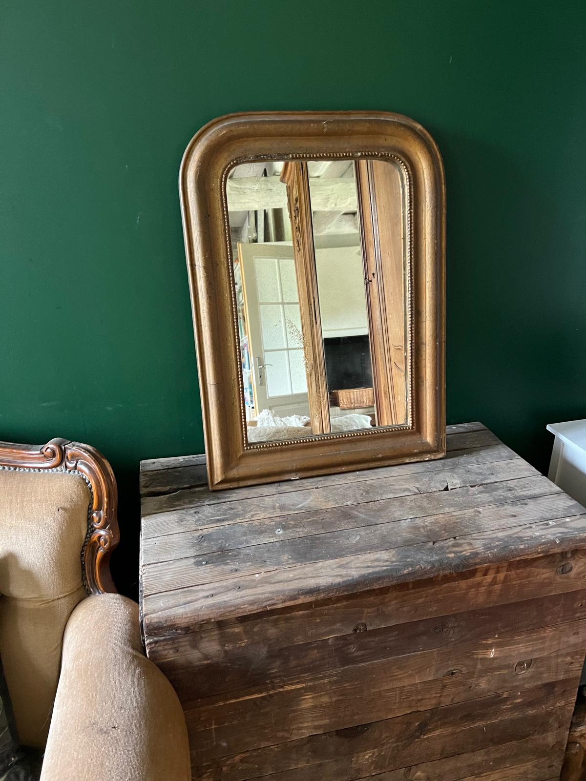 La Ferme Anglaise antique French Louis Philippe gilt mirror with beaded border and foxed glass on a wooden chest.