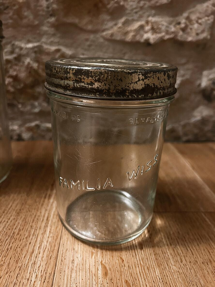 La Ferme Anglaise vintage Familia Wiss glass jar with a tarnished gold-tone metal screw lid on a wooden surface.